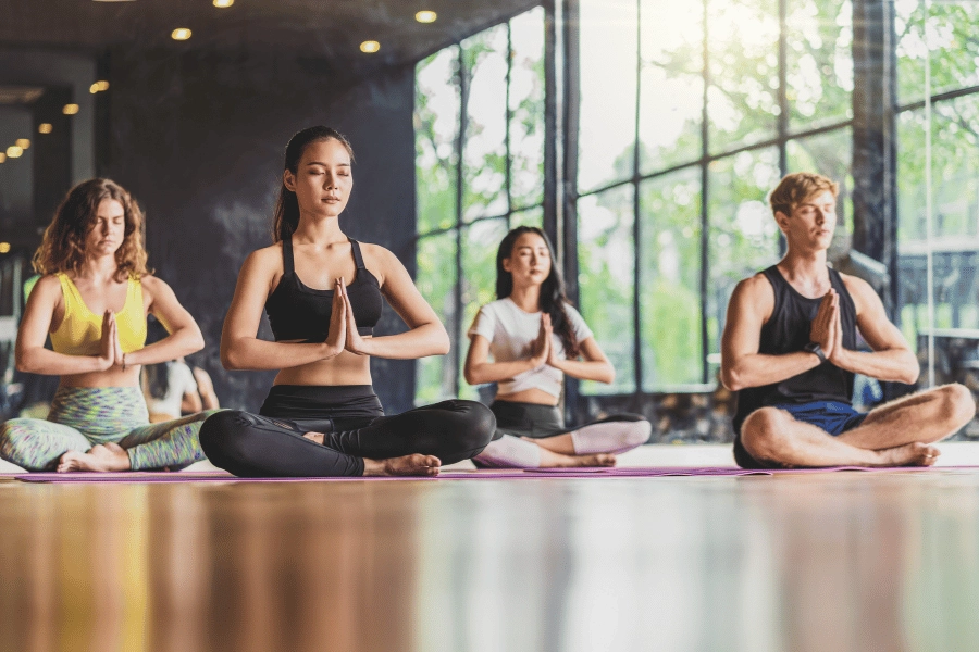 four students in a yoga class sitting with hands at their hearts and eyes closed